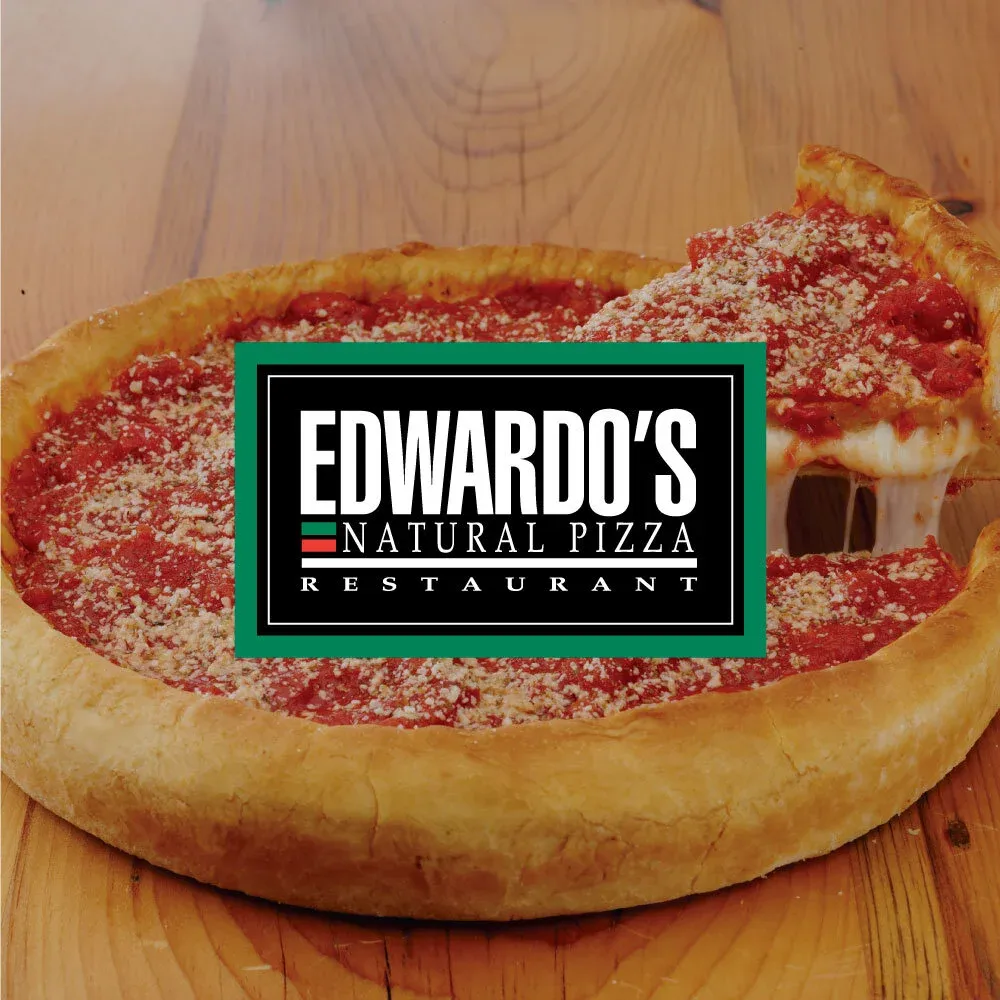A deep, cross-sectioned Edwardo’s stuffed pizza on a wooden table with a slice being pulled away.